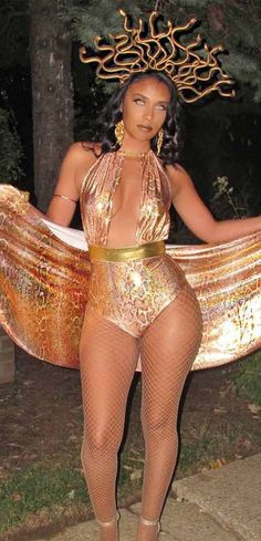 a woman in a gold bodysuit holding a large piece of cloth and posing for the camera