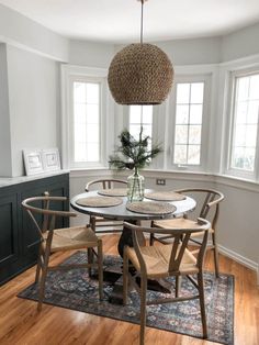 a dining room table with four chairs and a vase on top of it in front of two windows