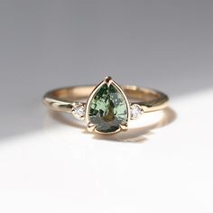 a pear shaped green tourmaline and diamond ring on a white surface with shadow