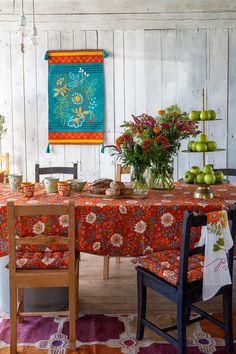 a dining room table covered in an orange and red floral cloth with potted plants on it