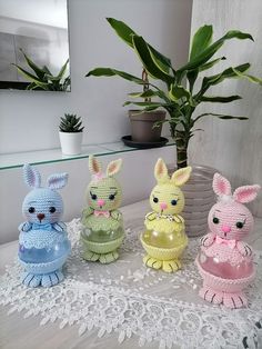 four crocheted rabbits sitting on top of a table next to a potted plant