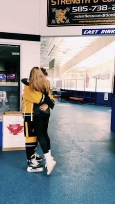 two people standing in an airport lobby hugging each other and looking at something on the ground