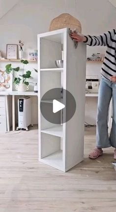 a woman standing next to a tall white bookcase on top of a hard wood floor