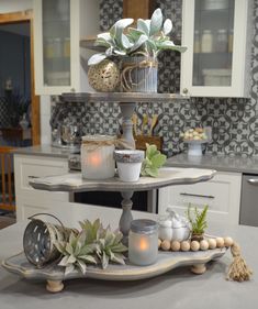 a three tiered tray with candles and plants on it in a kitchen next to an oven