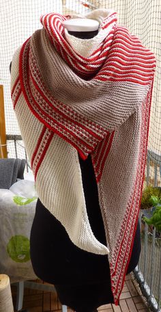 a red and white knitted shawl sitting on top of a mannequin