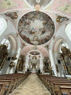 the interior of a large church with high ceilings and paintings on the walls, along with wooden pews