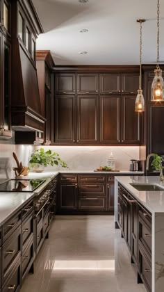 a kitchen with dark wood cabinets and marble counter tops, lights hanging from the ceiling