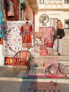 a woman standing in front of a store with lots of rugs and pillows on display