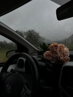 a bouquet of flowers sitting on the dashboard of a car in front of a rain soaked windshield