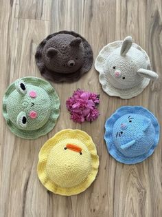 four crocheted animal hats sitting on top of a wooden floor next to flowers