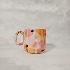 a pink and orange coffee cup sitting on top of a white table next to a wall