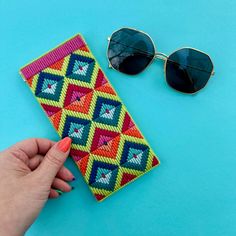 a woman's hand is holding a colorful wallet with sunglasses on the blue background