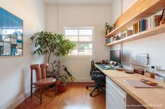 a room with a desk, chair and bookshelf filled with plants in it