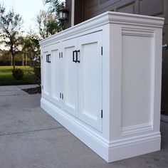 a white cabinet sitting on the side of a sidewalk next to a garage door and grass