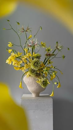 a white vase filled with yellow flowers on top of a table next to a gray wall