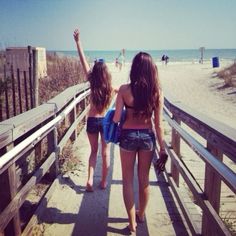 two young women walking down a boardwalk towards the beach