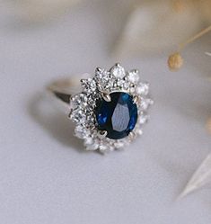 a blue and white diamond ring sitting on top of a table next to some flowers