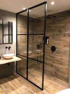 a glass shower door in a bathroom next to a white sink and wooden flooring