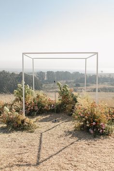 an outdoor wedding ceremony setup with flowers in the foreground and greenery on the far side