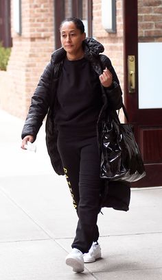 a woman walking down the street carrying a black bag and a handbag in her other hand