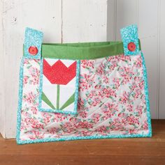 a small purse sitting on top of a wooden table next to a white door with a red flower in the pocket