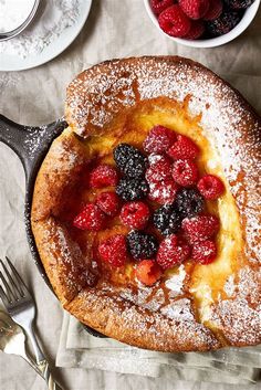 a cake with berries and powdered sugar on top next to other desserts, forks and spoons