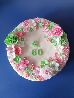 a birthday cake decorated with pink and green flowers on a blue tableclothed surface