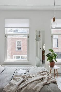 a bedroom with two windows and a bed in front of the window is covered by a blanket