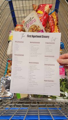 a person holding up a list in front of a shopping cart filled with food items