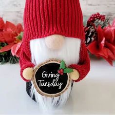 a gnome is holding a chalkboard with the words giving tuesday written on it and wearing a red knitted hat