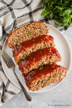 three slices of meatloaf on a white plate with a fork and parsley