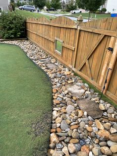 a wooden fence next to a grass covered yard with rocks and gravel on the ground