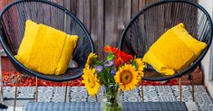 two chairs and a table with sunflowers on it in front of a wooden fence