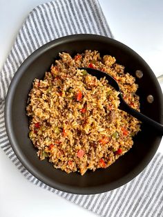 a skillet filled with rice and vegetables on top of a striped cloth next to a spoon