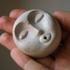 a hand holding a white ceramic object with two faces on it's face in the palm