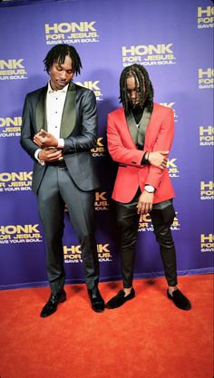 two men standing next to each other in front of a red carpet and blue wall