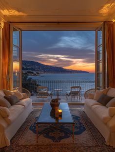 a living room filled with furniture and a large window overlooking the ocean at sunset or dawn