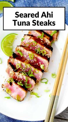 a white plate topped with meat and chopsticks next to a lime wedge on top of a wooden table