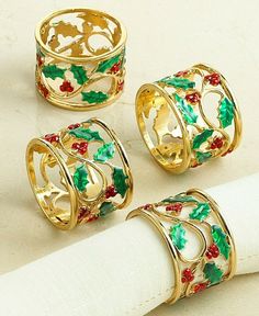 four christmas napkin rings with holly and mist design on them, sitting on top of a white napkin