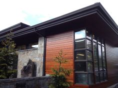 a house with wood siding and windows on the outside, along side a stone wall