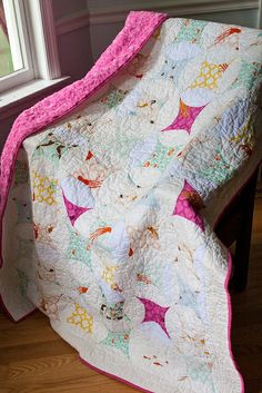 a pink and white quilt sitting on top of a wooden chair next to a window