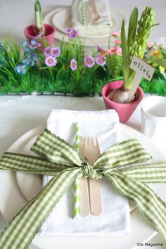 a place setting with green and white napkins, forks and flowers in the background