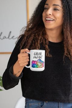 a woman with curly hair holding a white coffee mug in her right hand and smiling at the camera