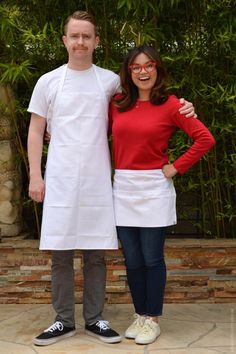 a man and woman standing next to each other in front of bamboo trees wearing white aprons