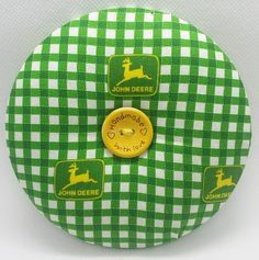 a green and white checkered pillow with a yellow button on the bottom that says john deer