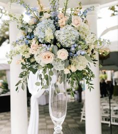 a tall vase filled with lots of flowers on top of a white table covered in chairs