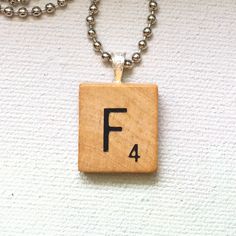 a wooden block with the letter f on it and a ball chain necklace attached to it