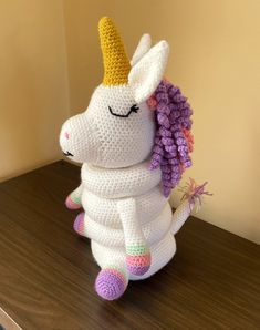 a crocheted stuffed unicorn sitting on top of a wooden table next to a wall