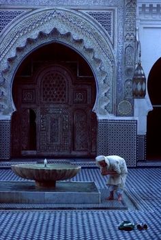 a man kneeling down in front of a fountain with the words fes garifyn mosque on it