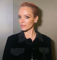 a woman with short hair wearing a black velvet jacket and diamond studded earring